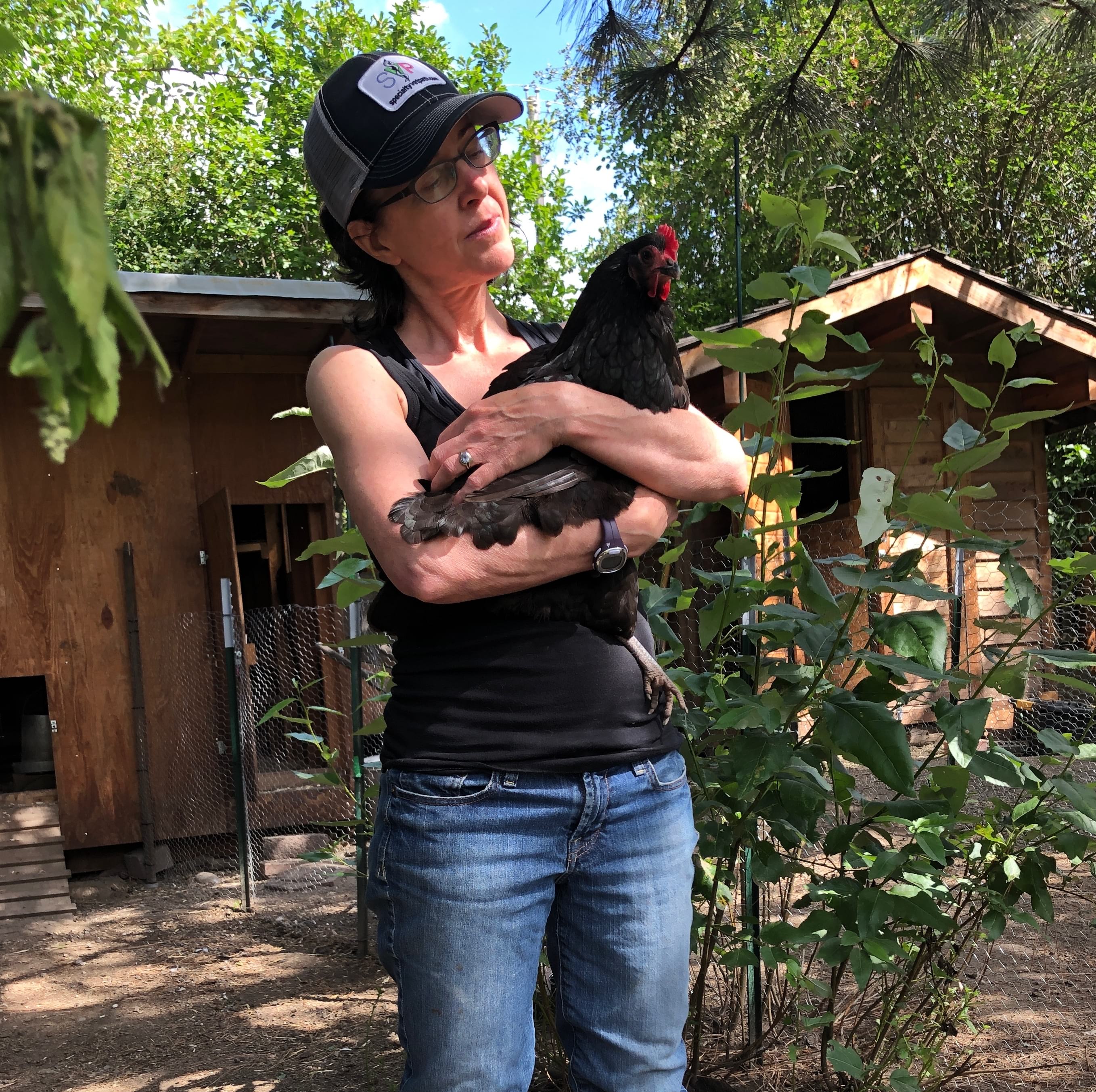 woman wearing glasses holding a black chicken in her arms